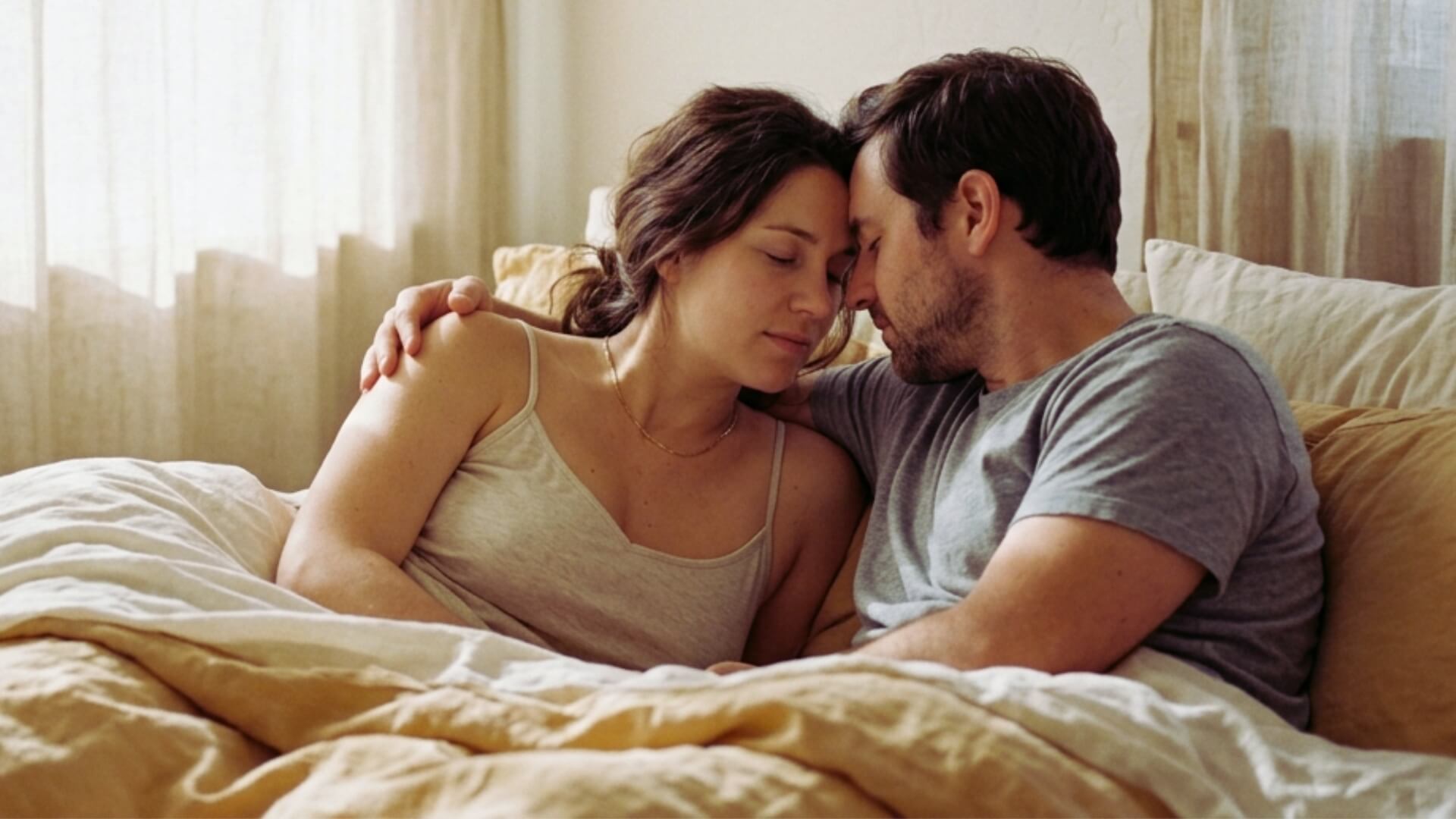 Couple allongé dans un lit, front contre front, dans une lumière douce — libido pendant et après la grossesse